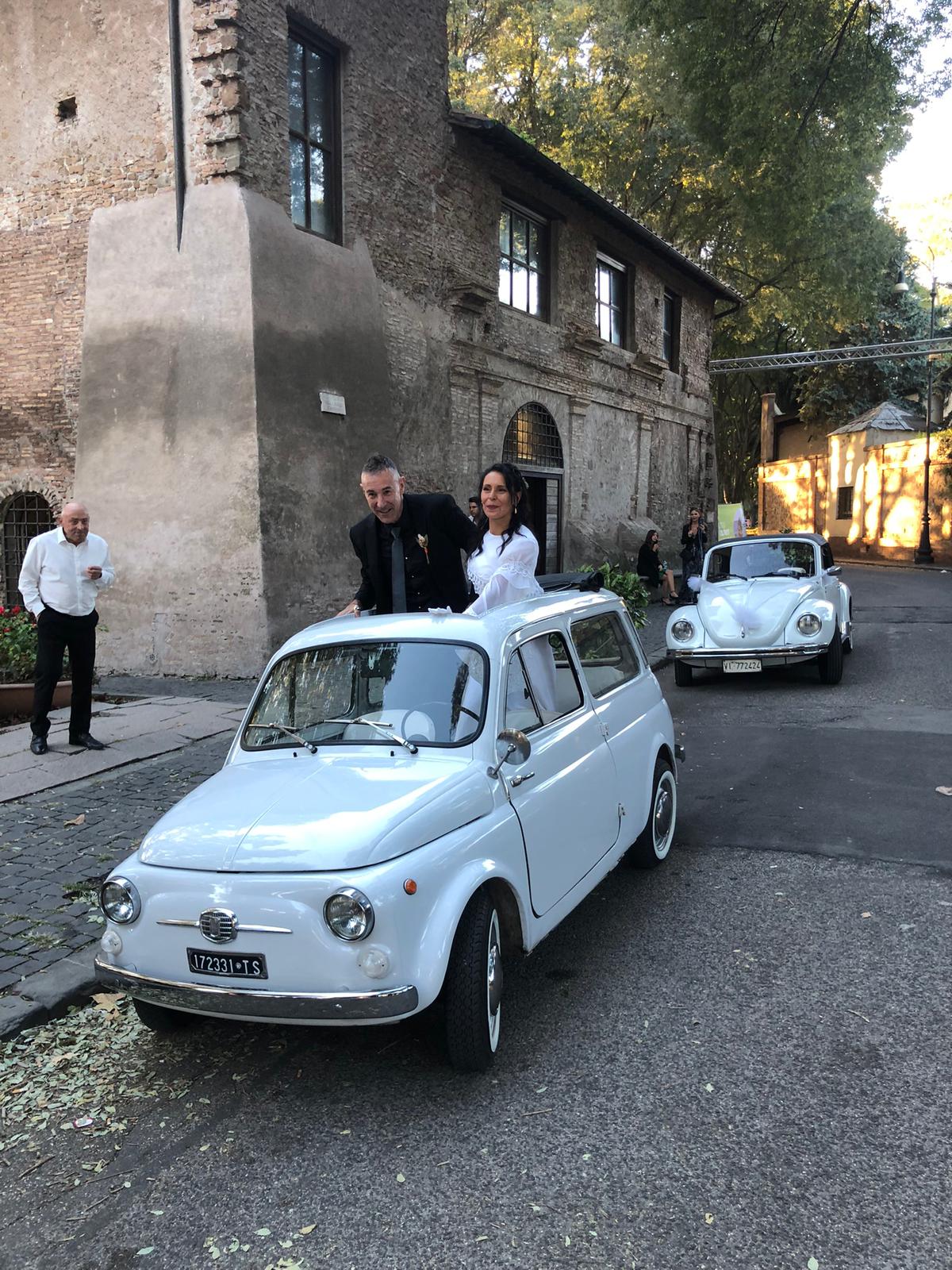 Bride and groom waving from a white vintage Fiat 500 convertible during a wedding