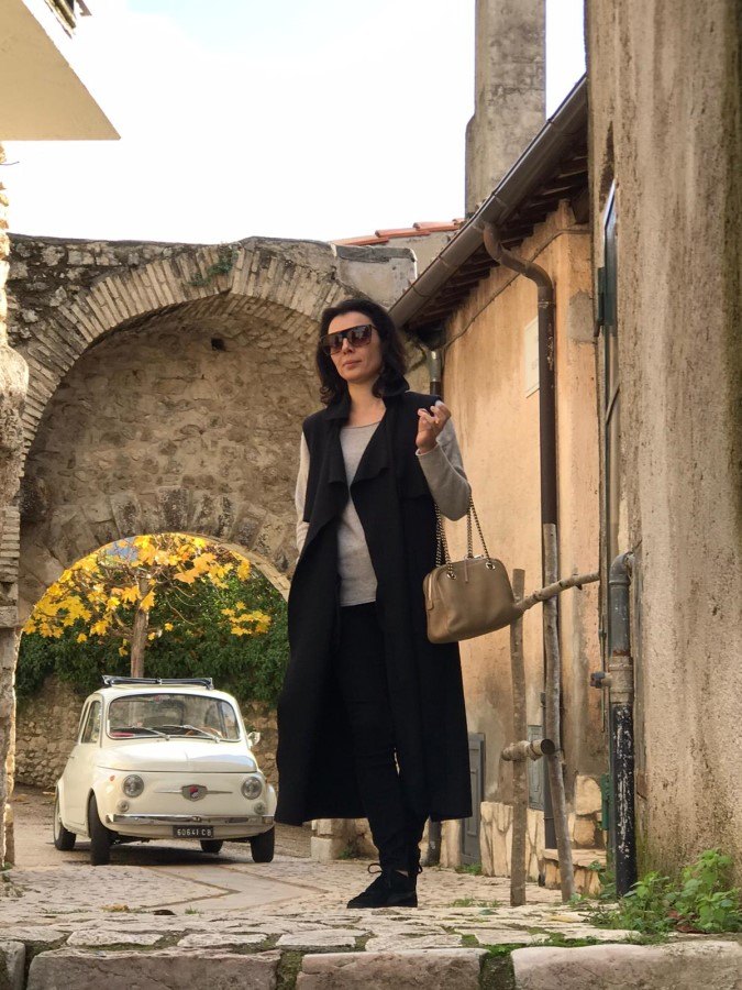Stylish woman in a Roman alleyway with a white vintage Fiat 500 parked under a stone archway