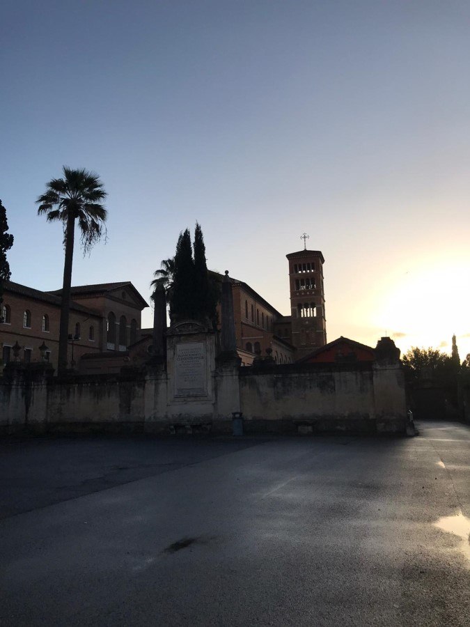 Silhouette of a Roman church bell tower against an orange and blue sunset sky